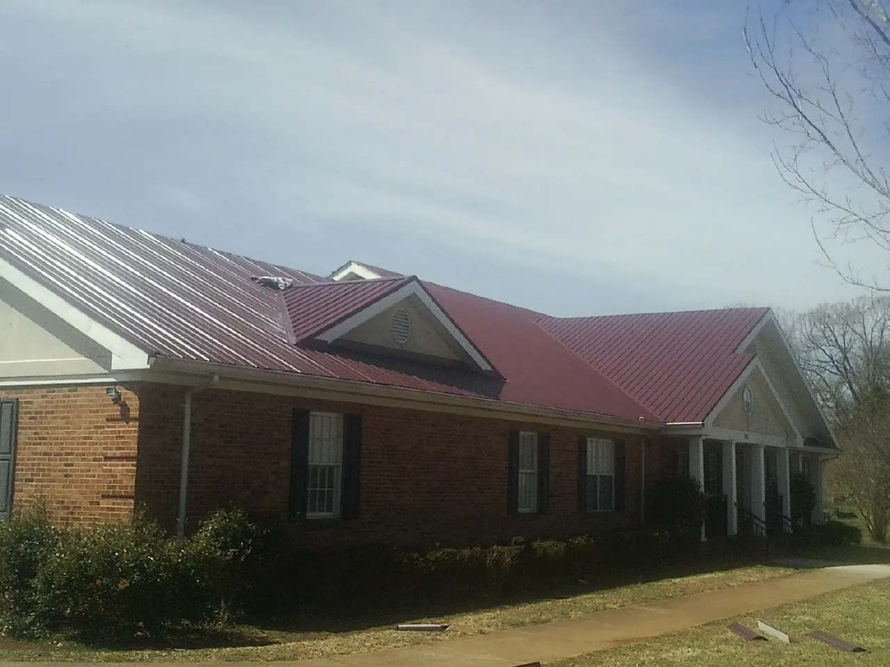 Red metal roof with gabled entries on a long brick building, from a Hail Damage Roof Repair job in Catskill