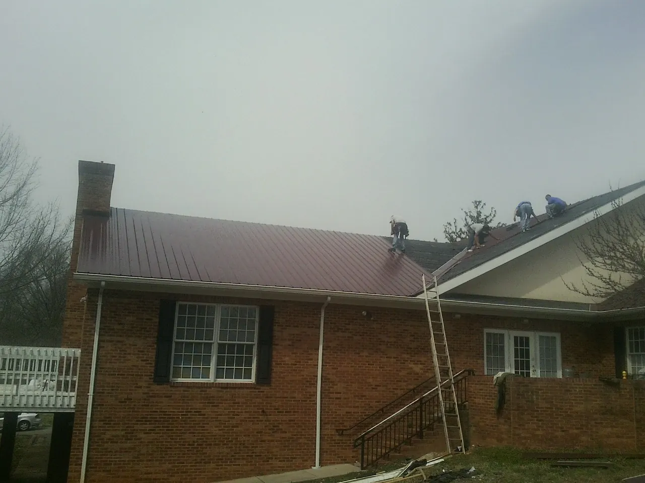 Crew setting red metal roofing panels on a brick home in Catskill
